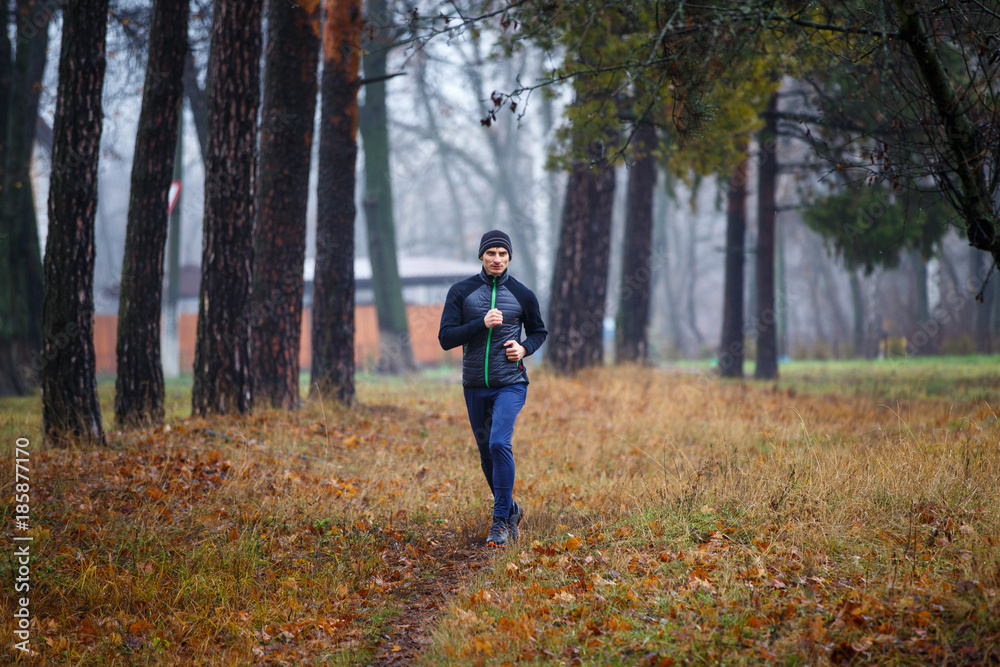 Young man jogging in fall park. Trail running in cold and misty weather Young man jogging in fall park. Trail running in cold and misty weather