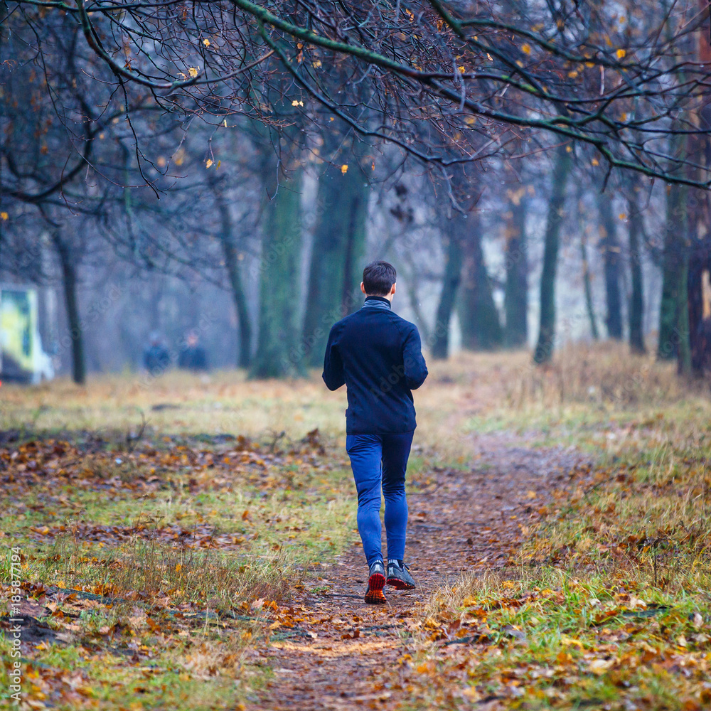 Young running man in fall park. Jogging in cold and misty weather