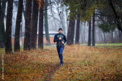 Young man jogging in fall park. Trail running in cold and misty weather
