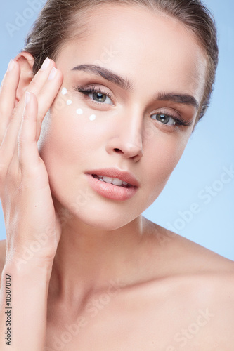 Young woman applying cream under eyes