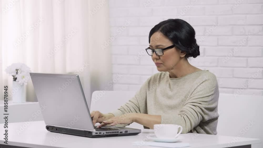 Adult asian female wearing glasses, typing on laptop, sending email to daughter Adult asian female wearing glasses, typing on laptop, sending email to daughter