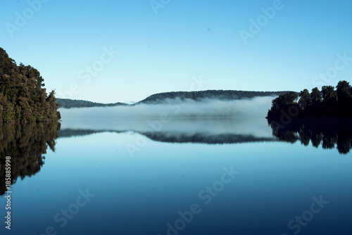 Lago en calma con reflejo de niebla y árboles.