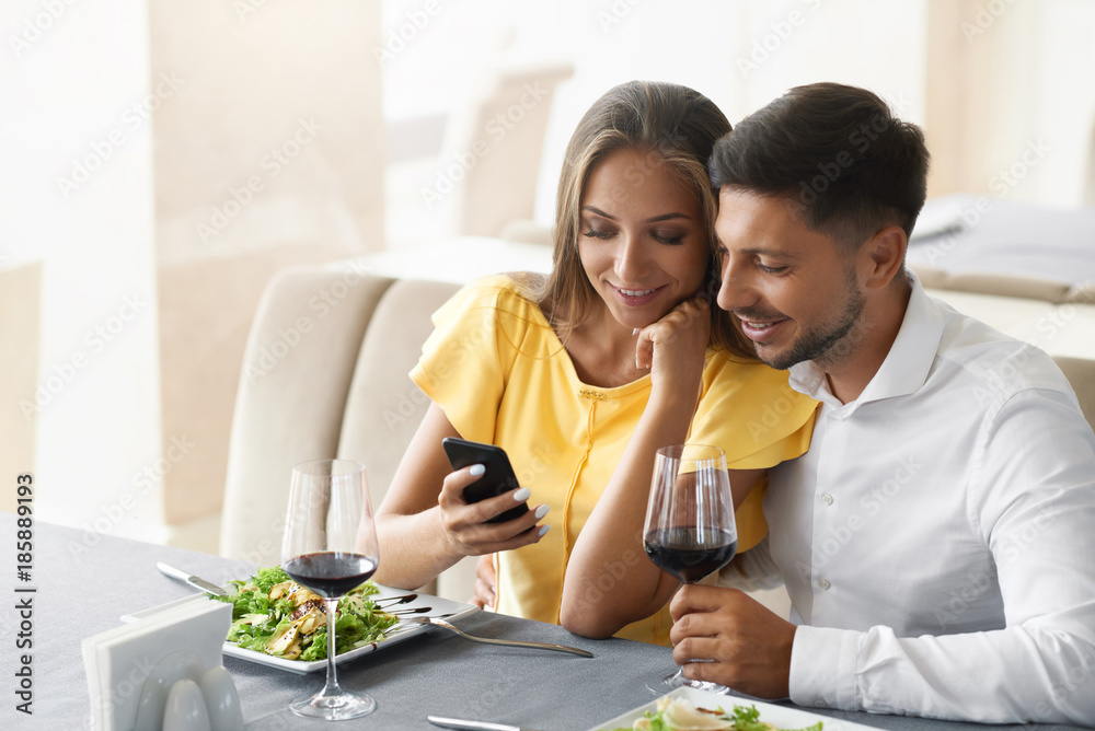 Couple In Love Looking On Phone Having Dinner In Restaurant. Couple In Love Looking On Phone Having Dinner In Restaurant.