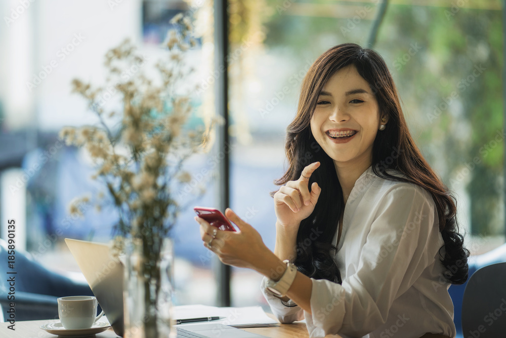 Portrait of an attractive young woman holding her phone while working in coffee shop.	