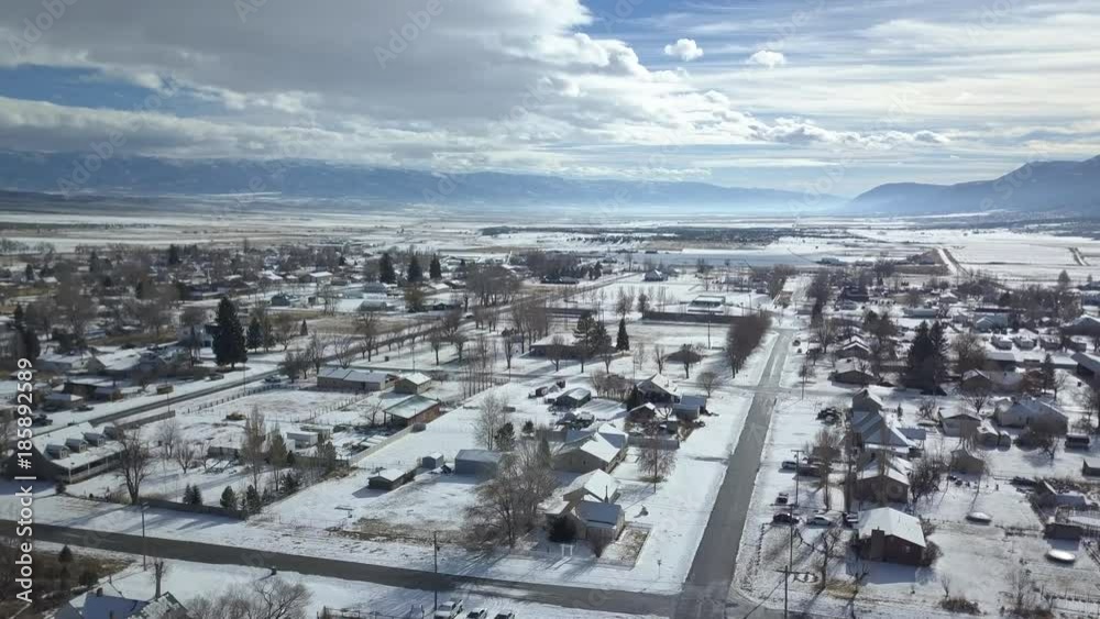 Aerial rural town winter snow mountain valley park school. Rural farm community. Homes, barns and buildings covered with white. Trees and fields covered and cold.