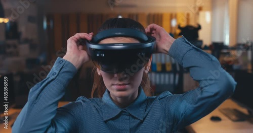 Young Caucasian female professional puts on augmented reality AR hololens headset in modern office. 4K UHD photo