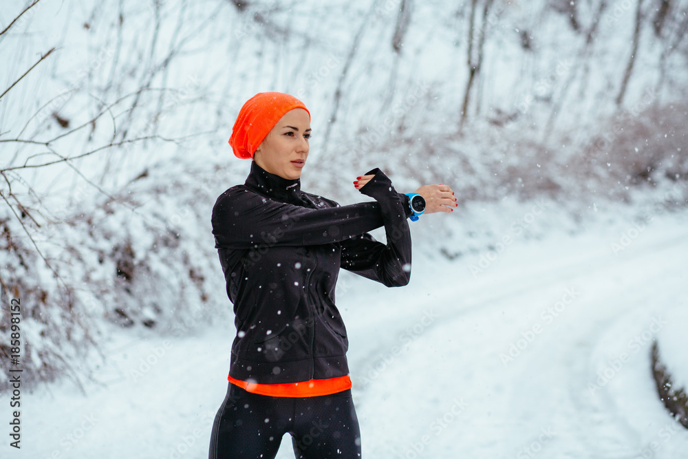 Outdoor sport exercises, sporty outfit ideas. Woman wearing black sportswear  training exercising stretching hands outside during winter. Snowfall Stock  Photo