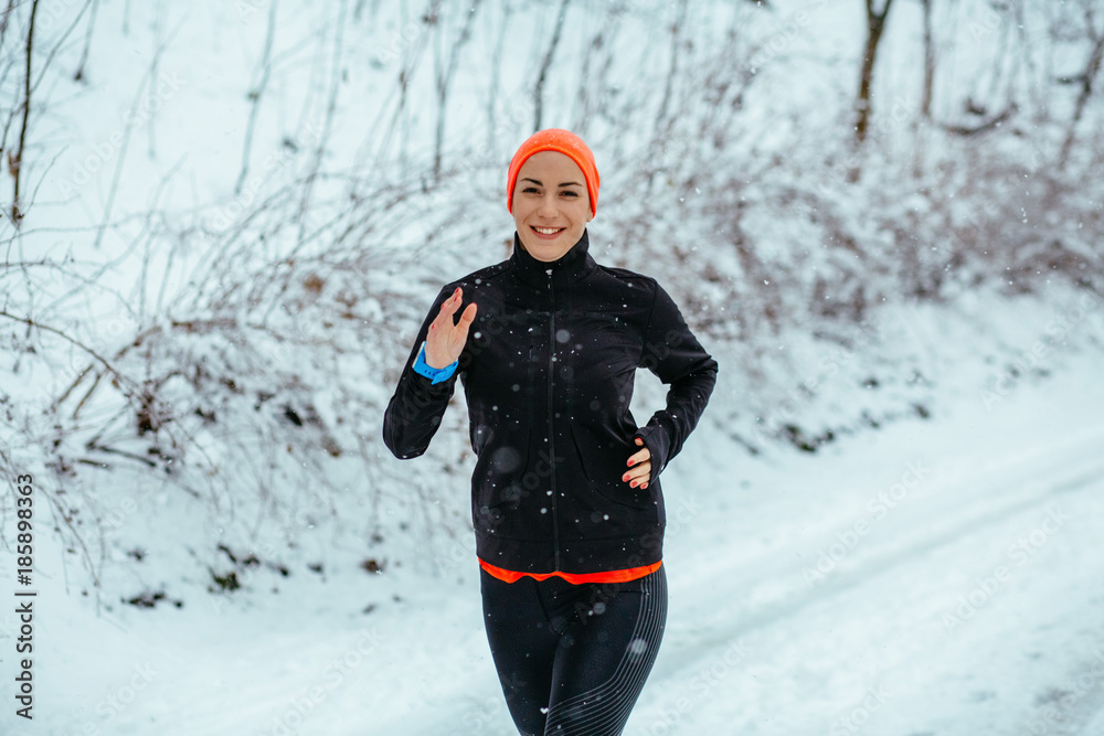 Young woman running in winter park at snowy day. Healthy lifestyle and cold weather concept.