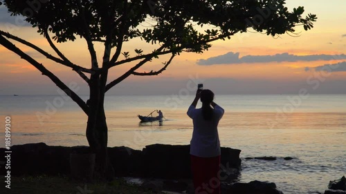 The woman photographs a decline with the boat on the smartphone. Boat on open sea sunset horizon.