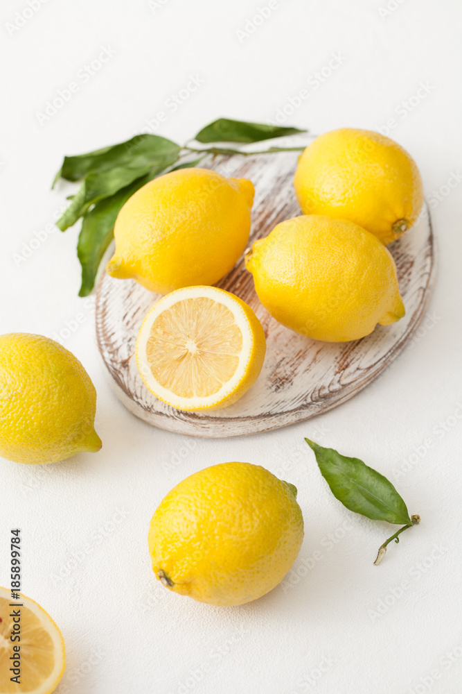 A bunch of lemons with leaves and sliced lemons on a white concrete background.