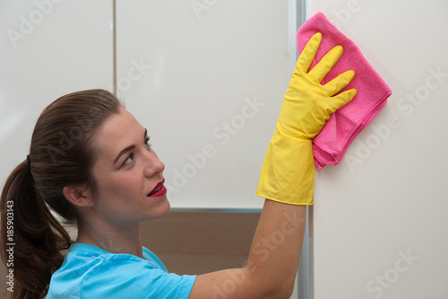 Positive employee of  cleaning company in gloves wipes furniture from dust with rag