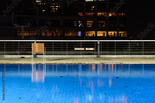 Wooden chairs are located at the hotel's swimming pool at night. © Vatcharachai