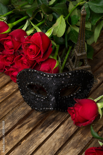 red fresh roses with black masque on wooden table photo