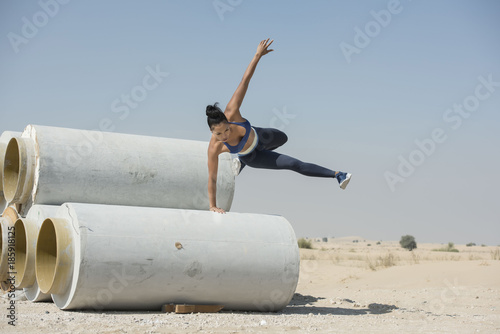 Принти на полотні Black African Amercian athletic woman jumps over and leaps from construction pipes wearing sports outfit in a parkour or extreme fitness competition wearing a sports outfit