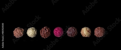 Verschiedene Schokoladentrüffel in einer Reihe - Isoliert auf schwarzem Hintergrund. 