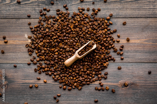 Scattered coffee beans and beans in scoop on dark wooden table top view. Coffee background.