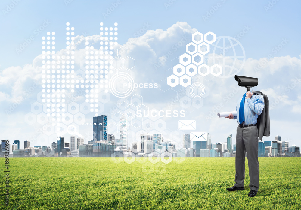 Camera headed man standing on green grass against modern cityscape Camera headed man standing on green grass against modern cityscape