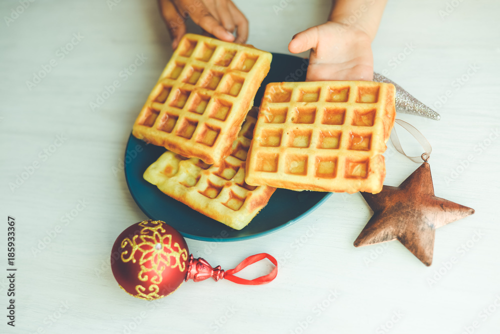 Closeup of child hand and baked waffles on light table background. Top side view on tasty natural decoration. Xmas classic lifestyle. Winter style delicious pastries.