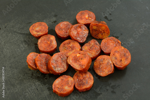 Bild auf Leinwand Sliced dried cured chorizo pork sausage on black cutting board as ingredient in
