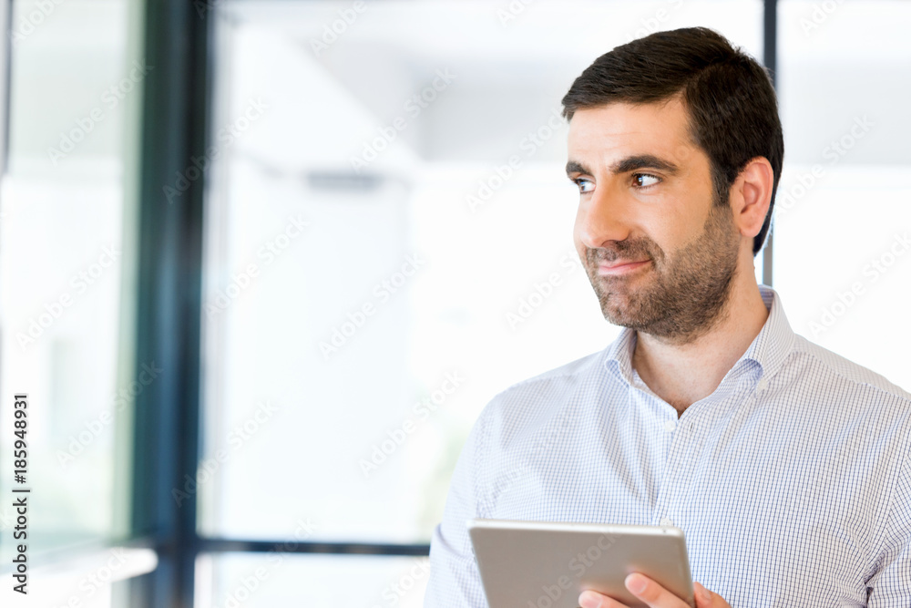 Young handsome businessman using his touchpad standing in office