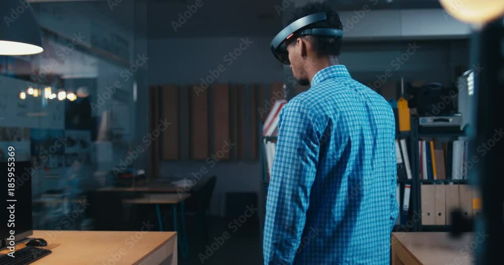 FIXED Back view of young adult African American black male using holographic augmented reality glasses in trendy office. Future concept. 4K UHD RAW edited footage FIXED Back view of young adult African American black male using holographic augmented reality glasses in trendy office. Future concept. 4K UHD RAW edited footage