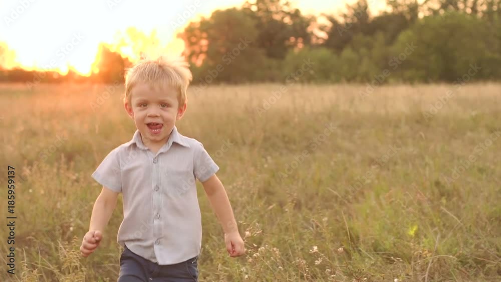 Little blond boy running on the grass in the Park at sunset, slow motion. Portrait of a beautiful little boy running through a field at sunset. Little blond boy running on the grass in the Park at sunset, slow motion. Portrait of a beautiful little boy running through a field at sunset.