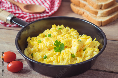 Scrambled egg in frying pan and toast on wooden table
