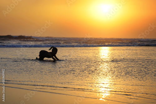 silhouette of anonymous unknown young girl on sea water playing happy and cheerful alone on the beach with wet sand