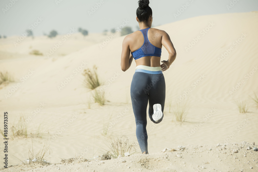 Rear closeup view of an athletic Black woman running in the hot dry desert  wearing long tight and a sports bra showing her midsection in an extreme  sports race. Stock Photo