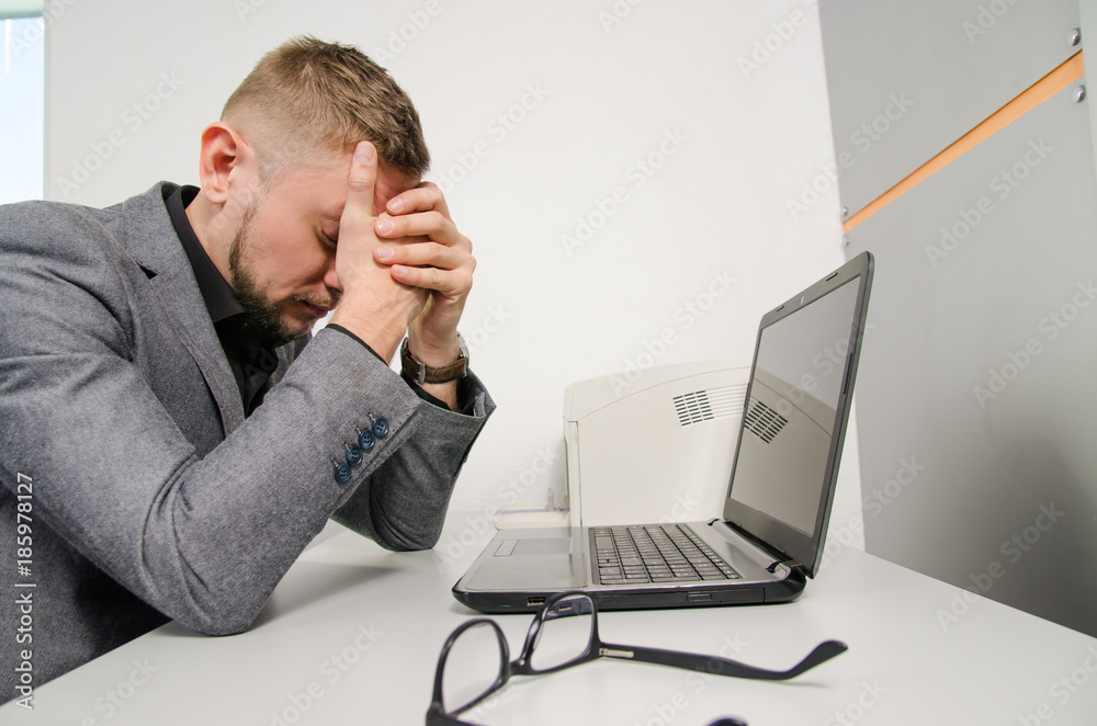 a tired man with his hands on the his face at the table with a laptop in the office a tired man with his hands on the his face at the table with a laptop in the office