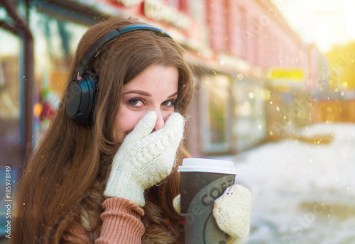 happy pretty woman in headphones listening to the nusic and drinking coffee on the street in winter time photo