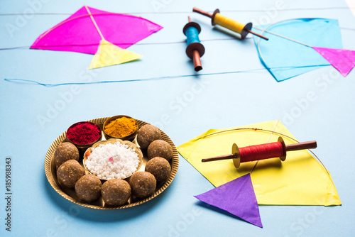 happy Makar Sankranti greeting card - Tilgul or Til ladoo in a bowl or plate with haldi kumkum and flowers with Fikri /Reel/Chakri /Spool with colourful thread or manjha and kite  photo