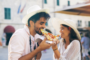 Happy couple of tourist eating pizza on street