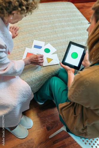 Female doctor showing geometric shape game to elderly female patient with dementia