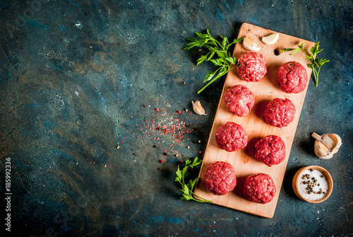 Raw meatballs with olive oil and spices on dark concrete table, top view copy space photo