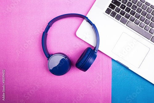 Blue headphones next to a laptop on two colored background. Flat style design. Top view