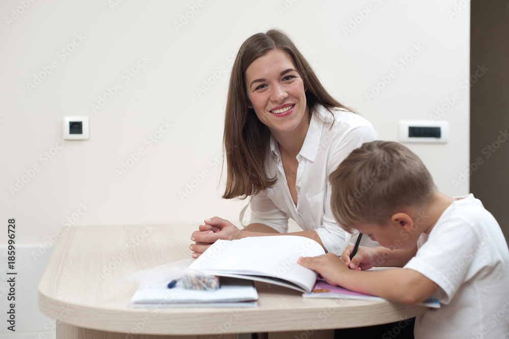 Happy beautiful young woman mother sitting next to her small child son painting coloring indoors Happy beautiful young woman mother sitting next to her small child son painting coloring indoors