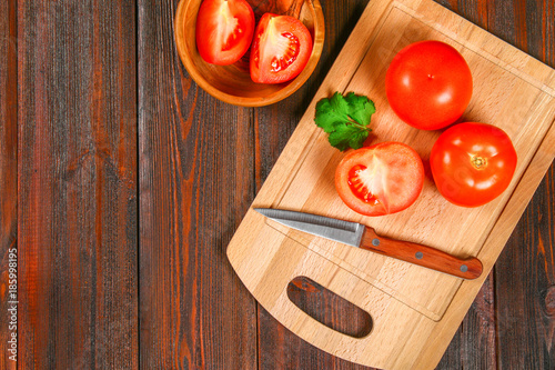 Fresh red tomatoes and sliced halves with cilantro on a wooden table. Top view.