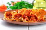 Traditional Italian pasta cannelloni. Baked tubes stuffed with minced meat with parmesan cheese and bechamel sauce on a white wooden table.