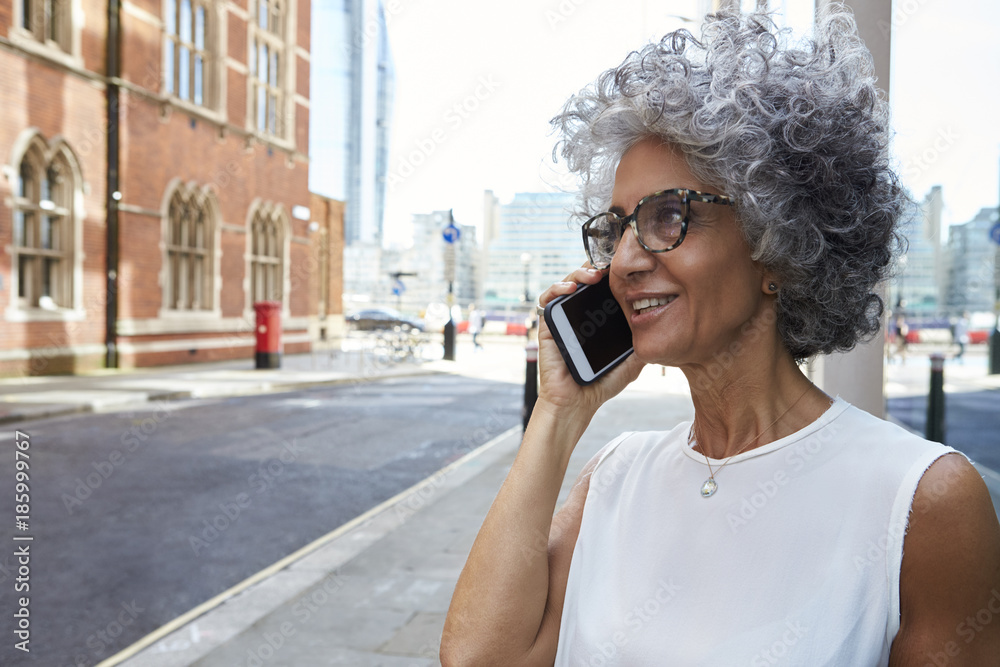 Fototapeta premium Middle aged woman talking on phone in city street, close up