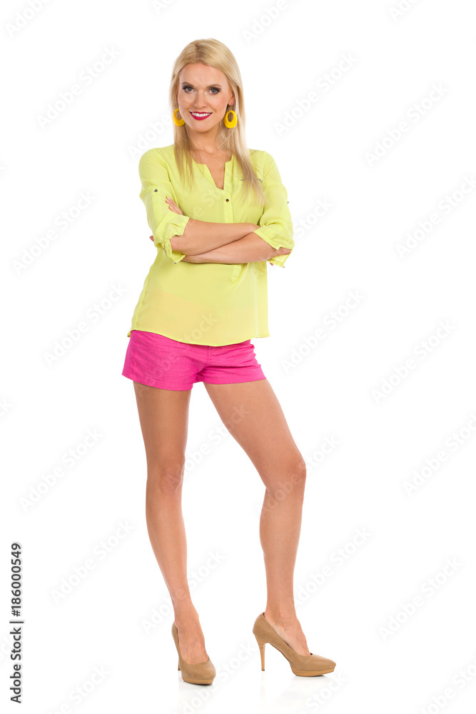 Smiling Beautiful Blond Woman In Vibrant Clothes And High Hells Is Standing With Arms Crossed And Looking At Camera Smiling Beautiful Blond Woman In Vibrant Clothes And High Hells Is Standing With Arms Crossed And Looking At Camera