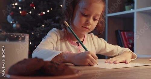 A pretty little girl drawing near a beautifully decorated Christmas tree hands merry christmas lights magic, message surprise kid letter slow motion photo