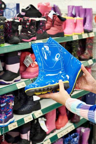 Childrens rubber boots in hands of buyer at store