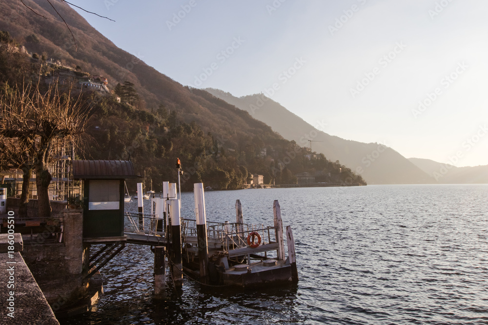 Small port of a town on Lake Como with storage of fishing boats and berth for ferries for public transport on the lake. Lights at sunset from the port of the village of Torno on Como Lake