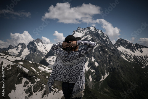 Boho woman wearing hat and poncho standing by the mountain.