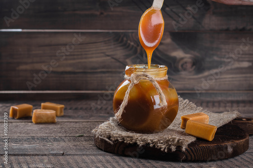 Homemade salted caramel sauce in jar on rustic wooden table background. Copy space. photo