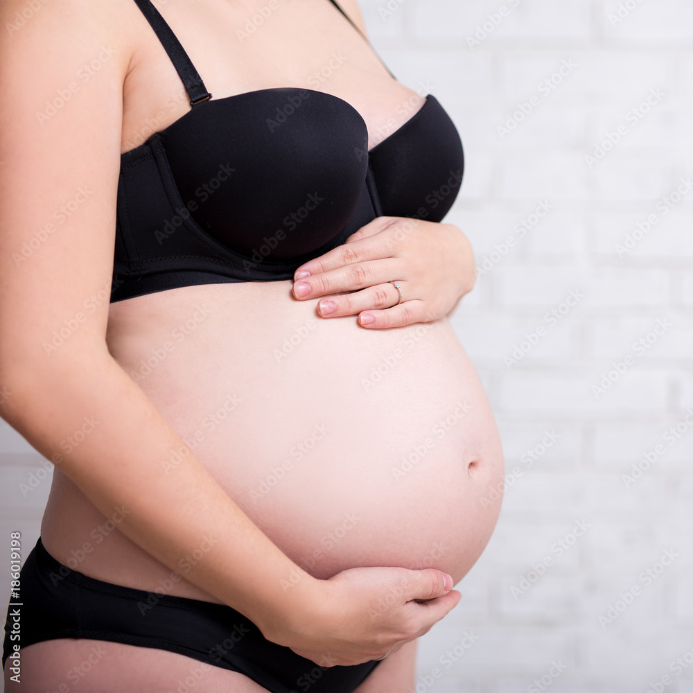 side view close up of belly of pregnant woman in lingerie over white wall  Stock Photo