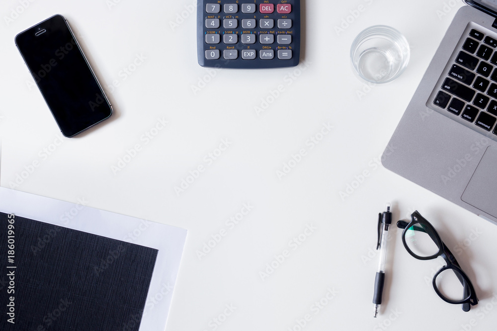 White office desk table with laptop, calculator, smartphone, file, and glass. Top view with copy space, flat lay. White office desk table with laptop, calculator, smartphone, file, and glass. Top view with copy space, flat lay.
