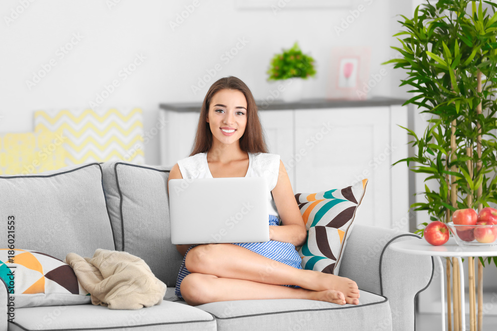 Young woman using laptop while sitting on cozy sofa indoors Young woman using laptop while sitting on cozy sofa indoors