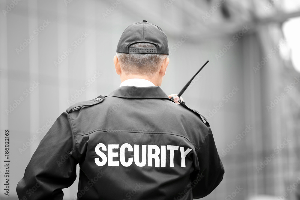 Male security guard using portable radio outdoors - obrazy, fototapety, plakaty 